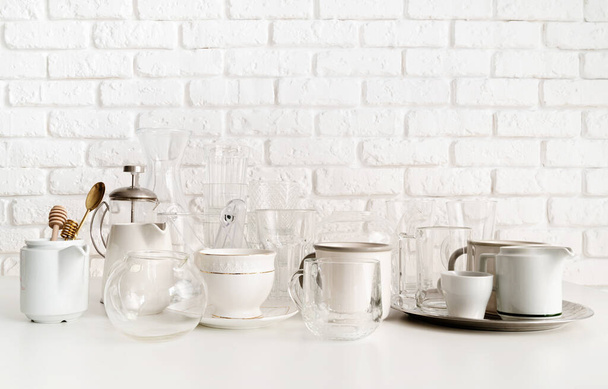 白いレンガの壁の背景のテーブルの上のセラミックとガラスのカップと食器 - 写真・画像