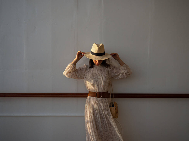 Jonge vrouw in een jurk en hoed aan de muur - Foto, afbeelding