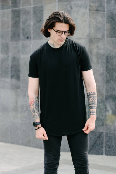 Handsome male model with beard wearing black blank t-shirt with free space for your logo or design in casual urban style - Foto, imagen