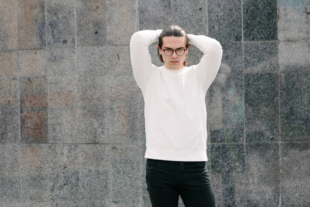 Man wearing white sweatshirt or hoodie and glasses outside on the city streets. Sweatshirt or hoodie for mock up, logo designs or design prints with free space - Φωτογραφία, εικόνα