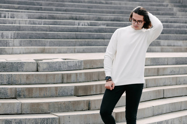 Man wearing white sweatshirt or hoodie and glasses outside on the city streets. Sweatshirt or hoodie for mock up, logo designs or design prints with free space - Photo, image