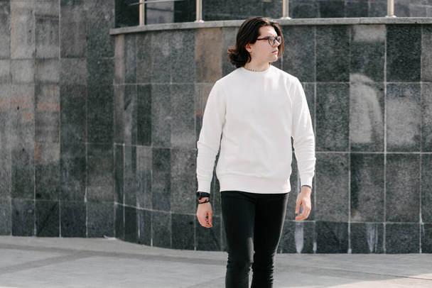Man wearing white sweatshirt or hoodie and glasses outside on the city streets. Sweatshirt or hoodie for mock up, logo designs or design prints with free space - Foto, Imagem