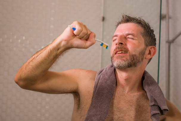 funny lifestyle portrait of young attractive and happy man with beard singing in the shower carefree and crazy at home with a toothbrush pretending holding a microphone enjoying - Foto, immagini