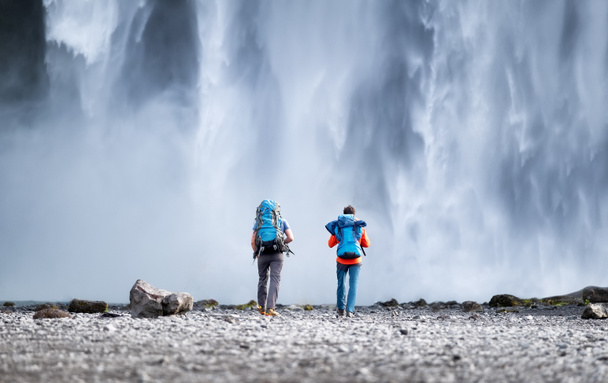 Reisendes Paar betrachtet den Skogafoss-Wasserfall. Reise- und Aktivlebenskonzept mit Team. Abenteuer und Reisen in Island. - Foto, Bild