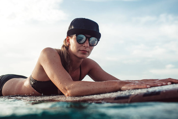 Beautiful girl posing sitting on a surfboard in the ocean. On the wonderful island of Bali - 写真・画像