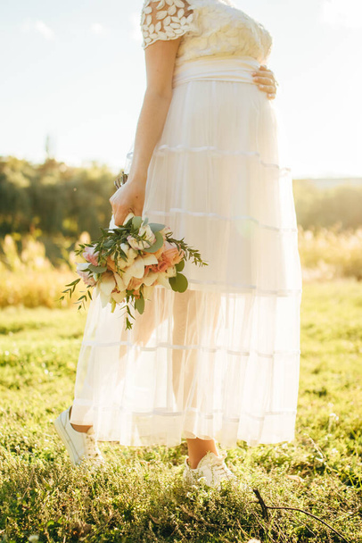 gyönyörű és gyengéd menyasszony tartja az esküvői csokrot a kezében, a háttérben a tenger és a naplemente. - Fotó, kép