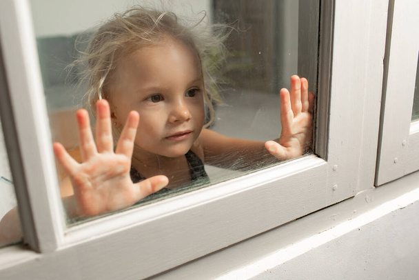 close-up view of adorable little girl leaning at glass and looking through window - Foto, immagini