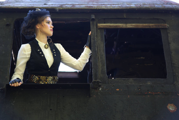 Een jonge vrouw in een retro pak staat in het rijtuig van een oude locomotief en kijkt weg. Historische wederopbouw - Foto, afbeelding