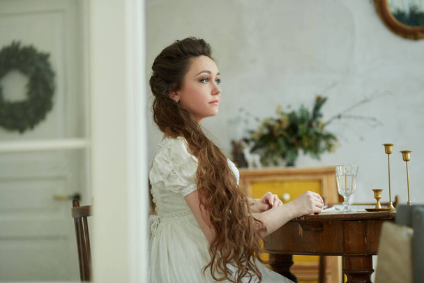 Красива жінка з довгим волоссям у довгій білій сукні. Він сидить за столом і дивиться вбік. Історична реконструкція
 - Фото, зображення