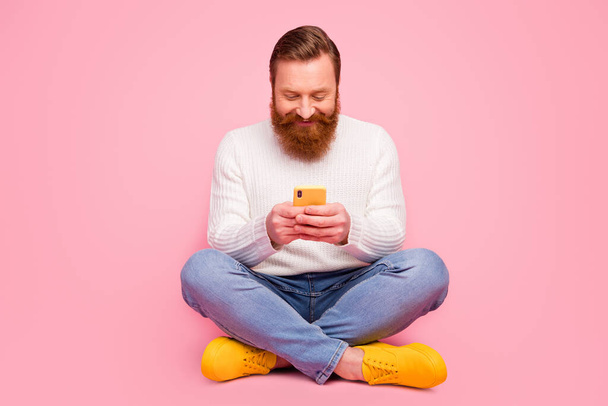 Full size photo positive cheerful guy hipster sit floor legs crossed use smart phone typing social network comment wear denim trendy style jeans white jumper isolated pastel color background - Fotoğraf, Görsel