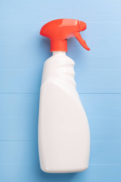Bottle of cleaning spray with a white case without inscriptions and a red bright dispenser on a wooden light blue background. Home wash product close-up. Vertical view - Photo, Image