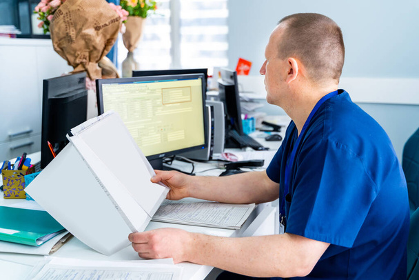 Male doctor in office looking at monitor. Reading results. Modern hospital office background. - Foto, imagen