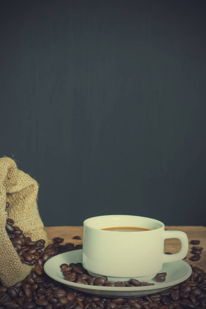 Kubek kawy i ziarna kawy w worku na drewnie stołowym. skopiuj miejsce na tekst. styl vintage. - Zdjęcie, obraz