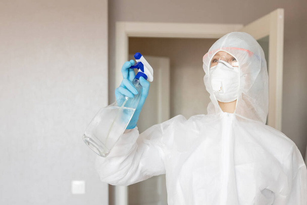 Kobieta pracownik dezynfekuje powierzchnię domu od infekcji wirusem i drobnoustrojami w biochemicznym garniturze - Zdjęcie, obraz