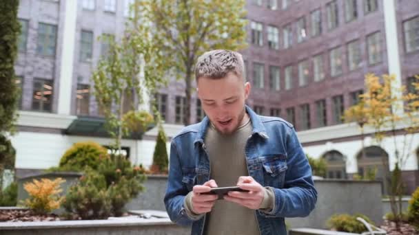 mladý muž hraje na telefonu na pozadí kancelářského centra - Záběry, video