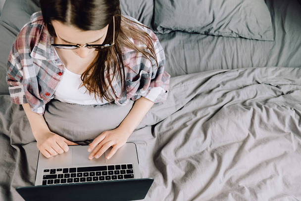 Top kilátás fiatal nő használ laptop ül az ágyban otthon, barna lány ellenőrzi a híreket a szociális hálózatok, dolgozik a számítógép, írás online blog vagy csinál internetes vásárlás. Szelektív fókusz - Fotó, kép