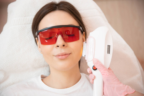 Master carries out removal of unwanted hair laser on face young woman. Health and beauty concept - Fotó, kép