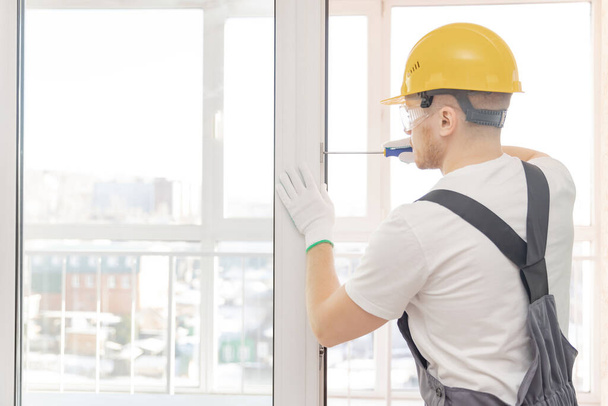 Worker man installs plastic windows white lock and seal adjustment - Fotó, kép