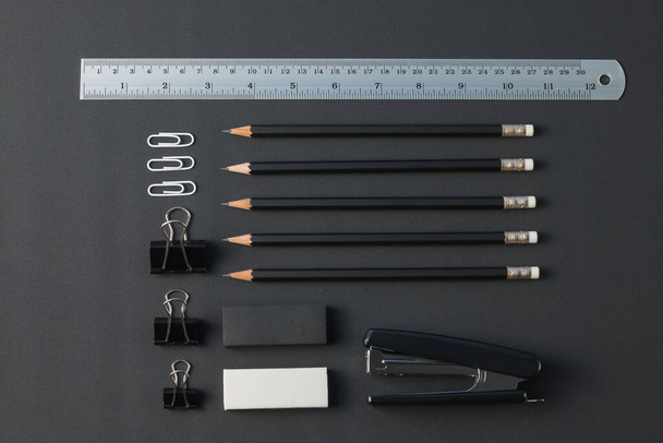 Kantoorbenodigdheden bovenaanzicht. met potloden, liniaal, gum, paperclip, nietmachine, op zwart bureau plat lay. - Foto, afbeelding