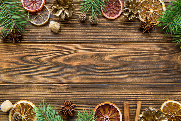 Αποξηραμένα πορτοκάλια, χρυσά χωνάκια και μπαχαρικά Χριστουγεννιάτικο φόντο. Καφέ ζάχαρη με γλυκάνισο αστέρια και ξυλάκια κανέλας σε καφέ ξύλινο φόντο. Χώρος για κείμενο. Άνω όψη.  - Φωτογραφία, εικόνα