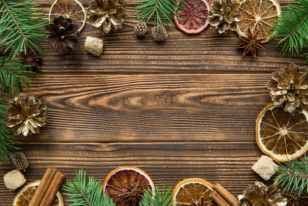 Christmas greeting background. Driend sicilian oranges, golden pine cones, spices, like anise and cinnamon, fir tree branches on brown wooden table background. Copy space, free space for text.  - Photo, image
