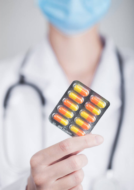 Doctor wearing blue face medical mask holding strip of pills on grey hospital wall background. Antibiotics and virus treatment tablet. - Φωτογραφία, εικόνα