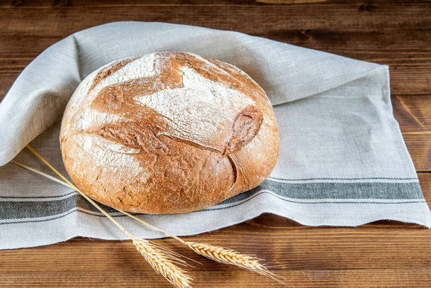 Broodje integraal brood op de keukenservet close-up. Spikeletten tarwe op de houten keukentafel. Gezonde voeding integraal brood.  - Foto, afbeelding