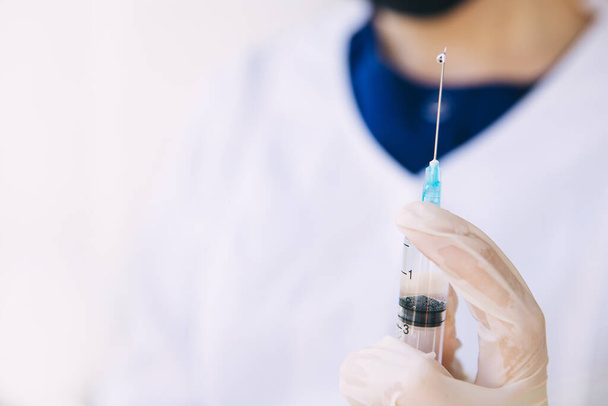 junge Ärztin in weißem Kittel und Operationsanzug mit einer medizinischen Spritze vor einer Injektion eines Coronavirus-Impfstoffs, Covid-19, Pandemie, Medizin, Quarantäne, 2020, Kopierraum - Foto, Bild