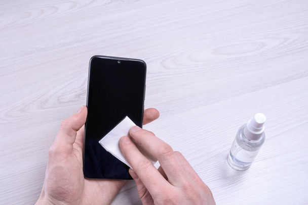 A man's hand holds and snaps a disinfectant spray and disinfect the phone to disinfect various surfaces that people touch.antibacterial antiseptic gel for hands - Foto, Bild