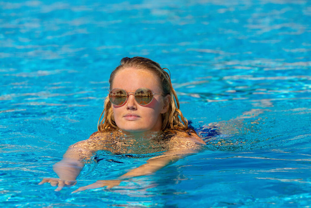 Young caucasian woman swims in blue water of outdoor swimming pool - Photo, Image