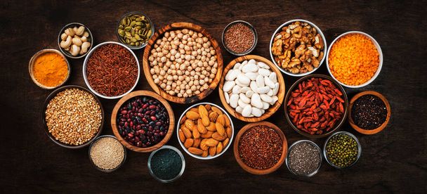 Superfoods, legumes, nuts, seeds and cereals set in bowls on wooden background. Superfood as chia, spirulina, beans, goji berries, quinoa, turmeric, mung bean, buckwheat, lentils, flax seed, wild rice and almond. Copy space, top view - Foto, imagen