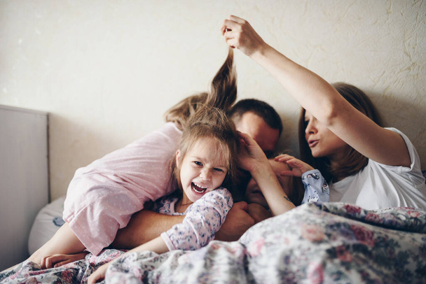 Children and parents rest in the morning in bed. Children indulge, hug. Twins. Three daughters. - Foto, Bild