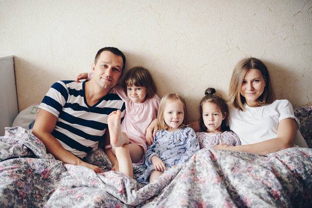 A gyerekek és a szülők pihennek reggel az ágyban. A gyerekek kényeztetnek, megölelnek. Ikrek. Három lány.. - Fotó, kép
