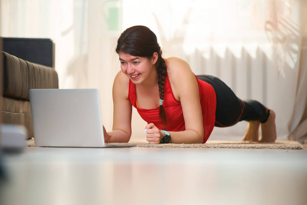 Frauen in sportlicher Trainingskleidung machen eine Brettübung, während sie Videotutorials nutzen. - Foto, Bild