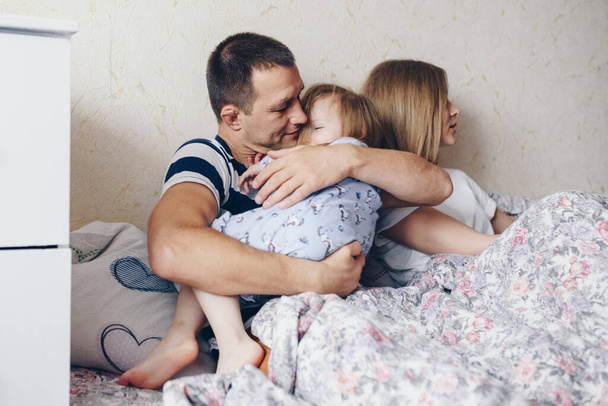 Girl and her parents rest in the morning in bed. They indulge, hug. - Fotografie, Obrázek