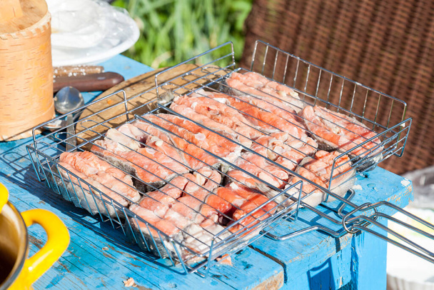 Steaks mit rotem Fisch - eingelegter Coho-Lachs auf einem Grill auf einem Tisch, der in der Hütte für Mai-Wochenenden für die ganze Familie zubereitet wird. Gesundes Essen im Freien zubereitet. - Foto, Bild