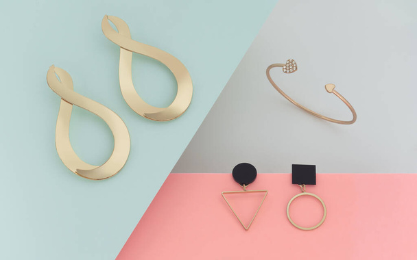Abstraktní dispozice moderních designových šperků. Zlaté náušnice a náramek na pastelové barvy pozadí papíru - Fotografie, Obrázek