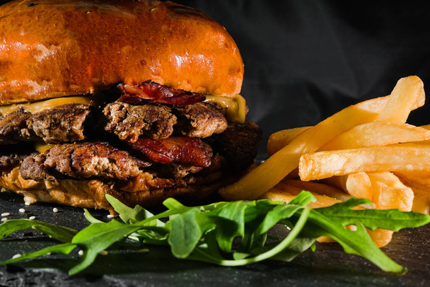 frietjes, hamburger met salade op een dienblad op een zwarte achtergrond. fastfood. Amerikaanse levensmiddelen rucola - Foto, afbeelding