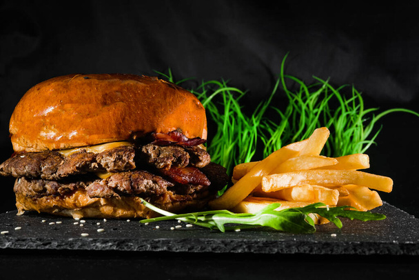 patatine fritte, hamburger con panino al sesamo e salsa su un bordo grigio di servizio su uno sfondo nero. fast food. cibo americano
 - Foto, immagini
