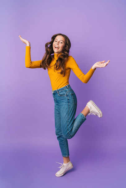 Full length image of young beautiful woman with long brown hair smiling and throwing up arms isolated over violet background - Foto, Imagem