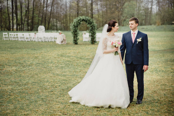 Wedding in the spring. Ceremony outside. An arch of real flowers. The bride and groom look at each other. - Photo, image