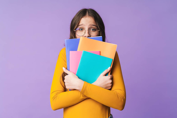 Image of young beautiful student girl wearing eyeglasses holding exercise books isolated over violet background - Foto, Imagen