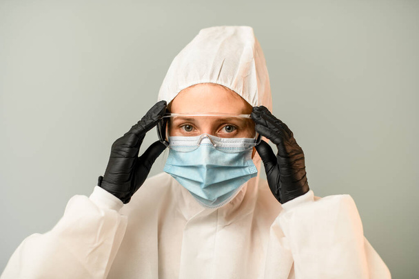 portrait of young woman in white protective suit with hood with surgical mask and protective glasses - Photo, image