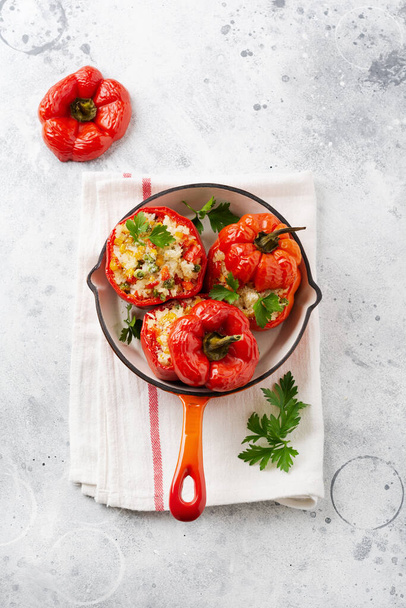 Red bell peppers stuffed with rice and vegetables on cast iron pan on gray concret background. - Фото, зображення
