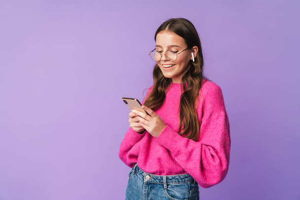Kuva nuori kaunis nainen yllään nappikuulokkeet hymyillen ja pitämällä matkapuhelin eristetty violetti tausta
 - Valokuva, kuva