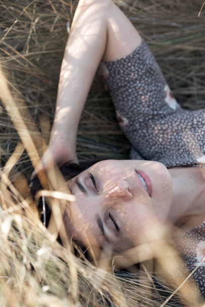 happy smiling girl lies in dry grass with closed eyes. retro style - Foto, afbeelding