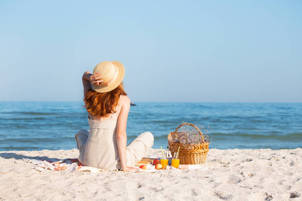Summer - picnic by the sea. Girl in Hat and basket for a picnic with buns, apples and juice. - Фото, изображение