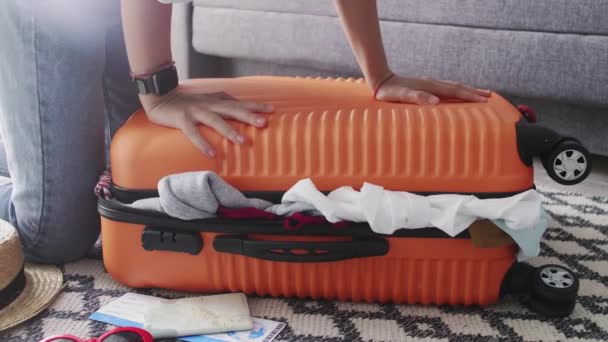 Nuori nainen seisoo polvillaan ylikuormitettu matkalaukku, yrittää sulkea sen - Materiaali, video