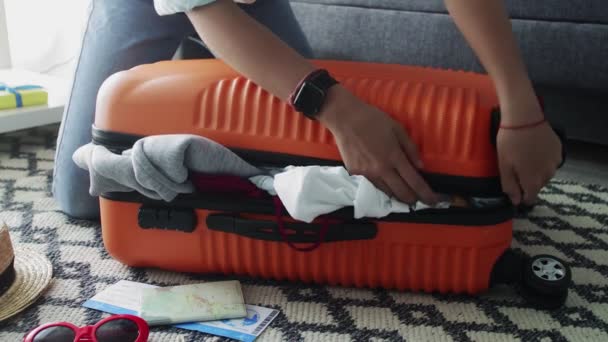 Söpö tyttö seisoo polvillaan ylikuormitettu oranssi matkalaukku, yrittää sulkea sen
 - Materiaali, video