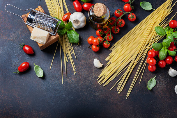 Concept of italian food: spaghetti, tomato, basil, garlic, cheese and olive oil on the black table. Top view with a copy space - Фото, зображення
